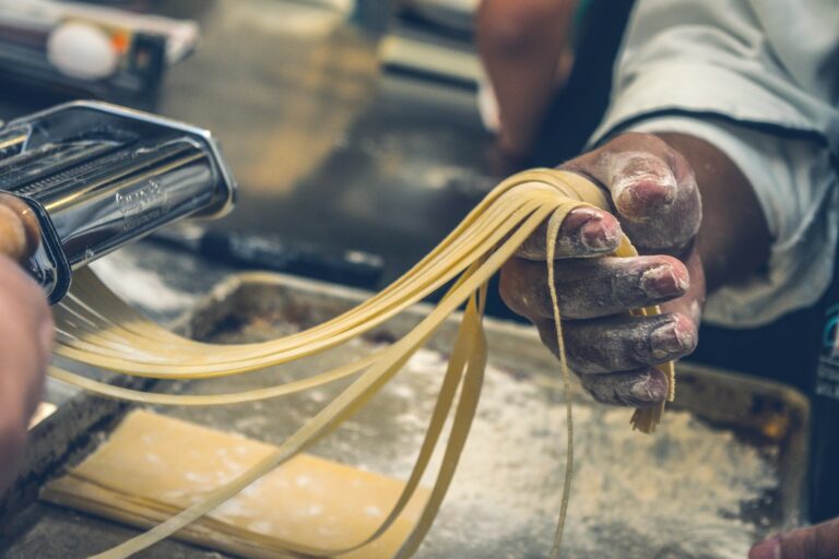 Un cuisinier tient des tagliatelles fraîches dans sa main farinée, sortant de la machine à pâtes du restaurant la table de 3 à Bordeaux.