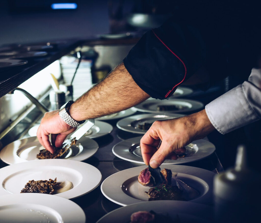 Gros plan sur deux avant bras de cuisiniers qui dressent délicatemeny des plats du restaurant la table de 3 à Bordeaux.