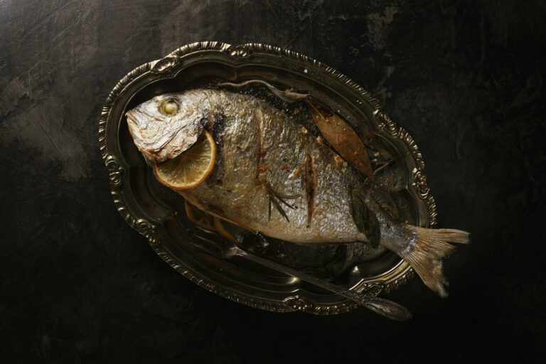 Poisson cuit au four présenté dans un plat en argent avec une rondelle de citron dans la branchie et une feuille de laurier du restaurant la table de trois à Bordeaux.