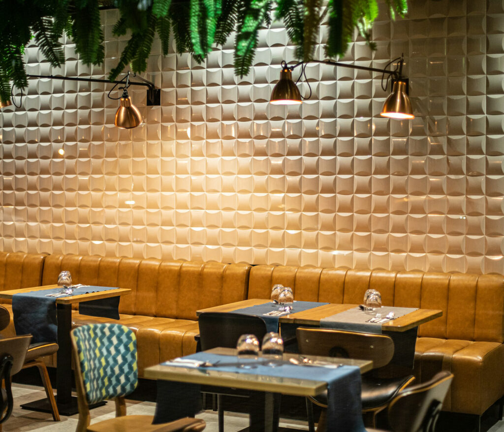 Salle de restaurant décorée avec des banquettes jaunes et des plantes au plafond à la table de trois à Bordeaux.