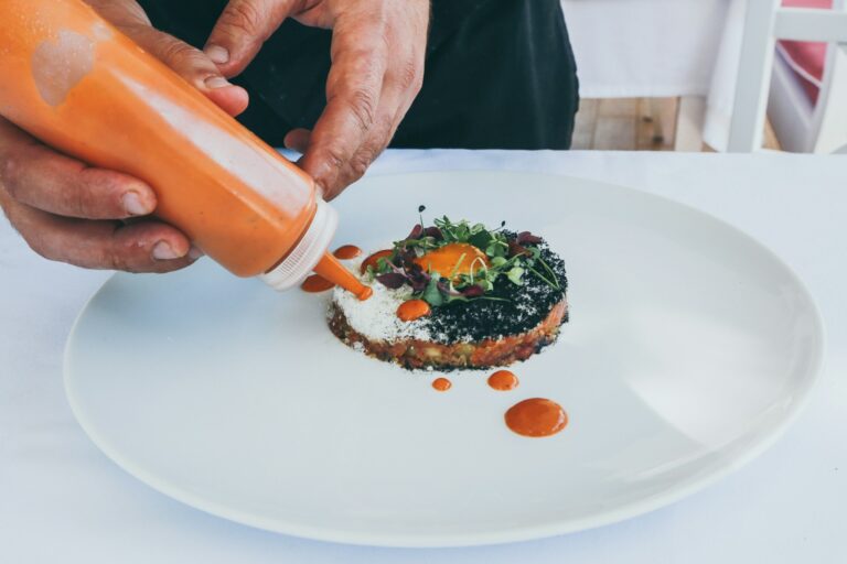 Un cuisinier applique des points de sauce orange dans une assiette au restaurant la table de trois à Bordeaux.